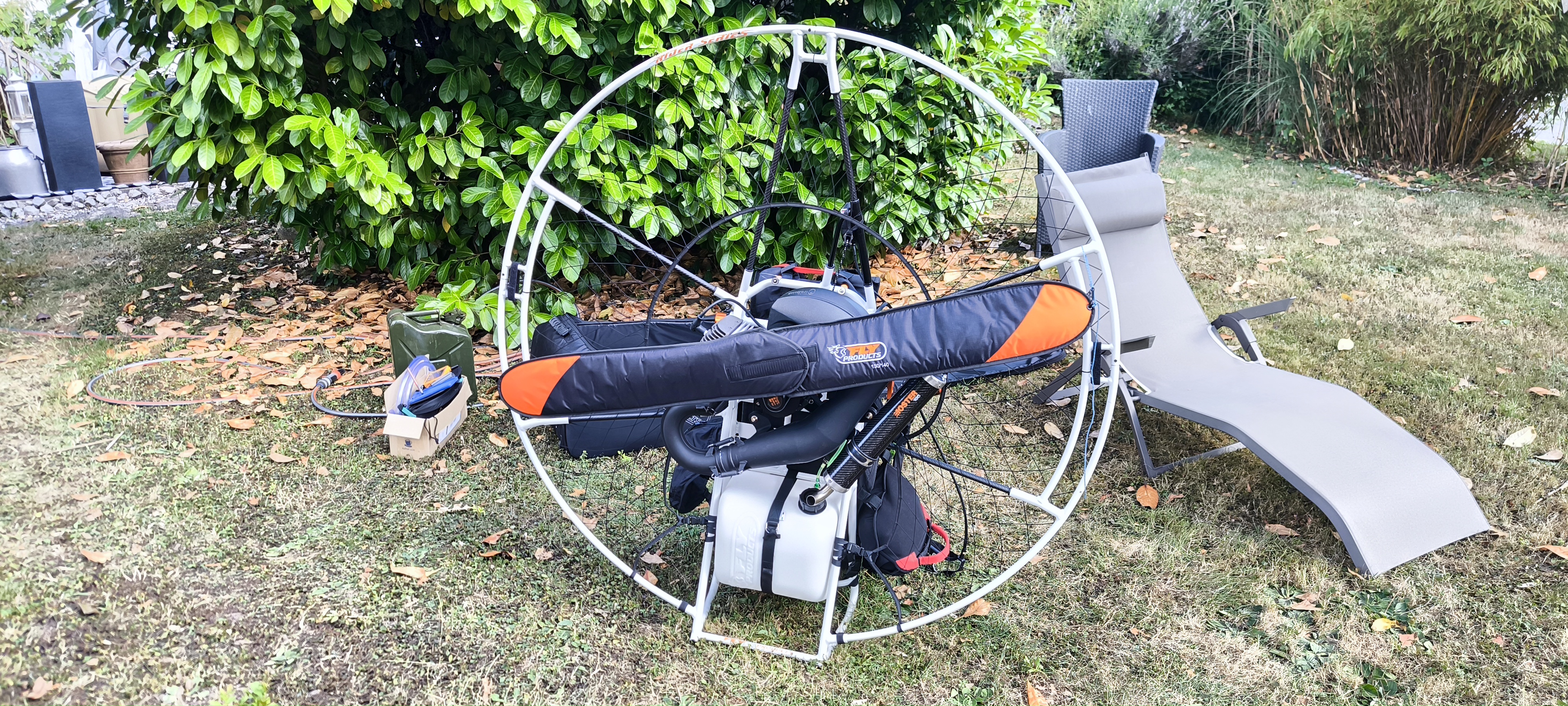 Ein Paramotor mit weißem Rahmen, schwarzem Motor und weißem Kraftstofftank steht auf einer Grasfläche. Das Bild hebt die Vorteile der Benzinkupplungen am Paramotor hervor, die sicheres Tanken und sauberen Transport ermöglichen.