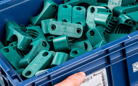 Stauff Kunststoff-Rohrschellen und Befestigungselemente Blaue Industriekiste gefüllt mit vielen grünen Kunststoff-Rohrschellen und Befestigungselementen der Marke Stauff.