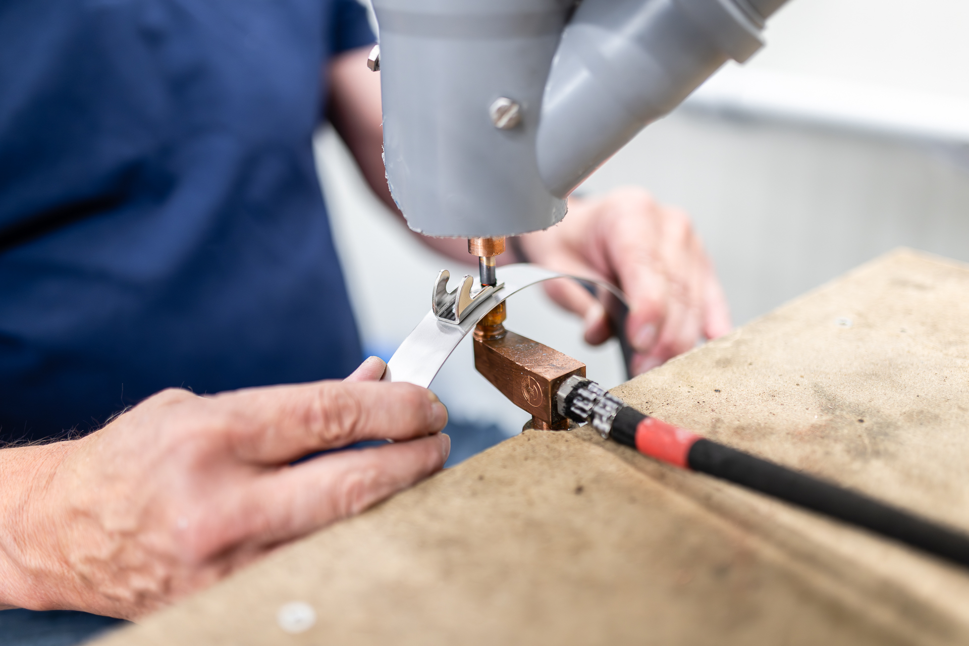 Professionelles Punktschweißen eines Metallbandes in der Fertigung. Nahaufnahme von Händen, die ein Metallband unter einem Punktschweißgerät auf einer Werkbank halten, während die Verbindung hergestellt wird.