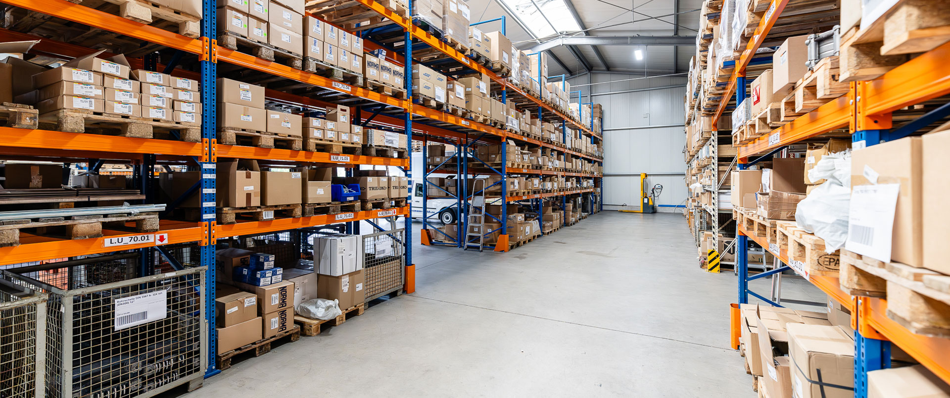 Über 10.000 verschiedene Artikel sofort lieferbar! Gang zwischen Lagerregalen im Schellen-Shop, die mit diversen Rohrschellen, Schlauchschellen und Rohrverbindern gefüllt sind