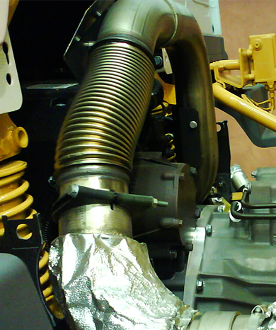 Detailansicht der Abgasrohrschelle / Auspuffschelle ARS aus verzinktem Stahl, zur sicheren und dauerhaften Verbindung von Auspuffkomponenten. Abgasrohrschelle / Auspuffschelle ARS aus verzinktem Stahl, montiert an einem flexiblen, gerippten Abgasrohr, das mit einem isolierten Auspuffteil verbunden ist.